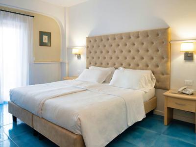 Bright hotel room with large bed, soft pillows, and bedside lamps.