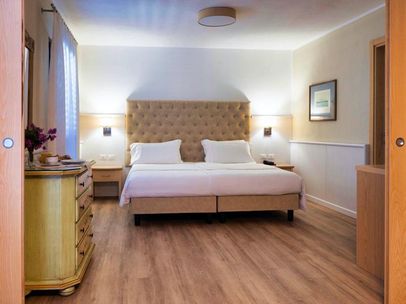 Bright hotel room with double bed, wooden floor, and dresser.