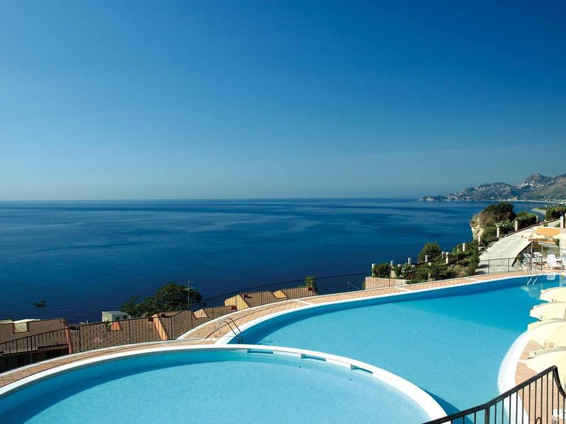 Rundlicher Pool mit klar blauem Wasser, Blick auf das Meer und Küste unter klarem Himmel.