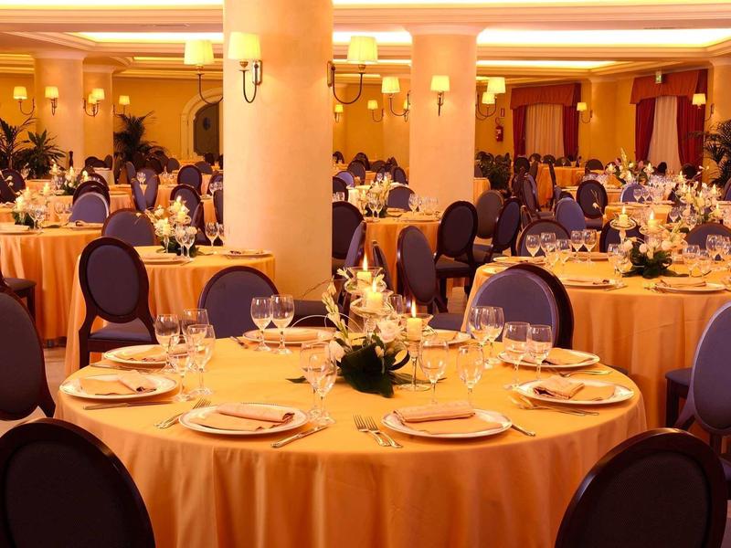 Festlich gedeckte runde Tische mit gelben Tischdecken und blauen Stühlen in elegantem Saal.