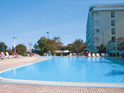 Grande piscine extérieure à côté d'un bâtiment d'hôtel à plusieurs étages sous un ciel ensoleillé.