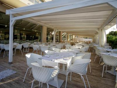 Grande terrasse extérieure avec chaises et tables blanches sous un auvent moderne.