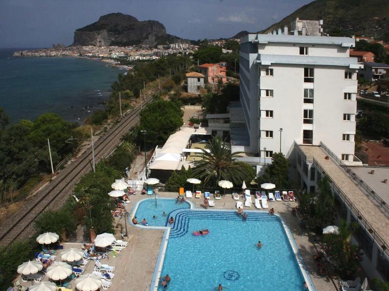 Espace piscine d'hôtel avec parasols, transats et vue sur la mer et les collines environnantes.