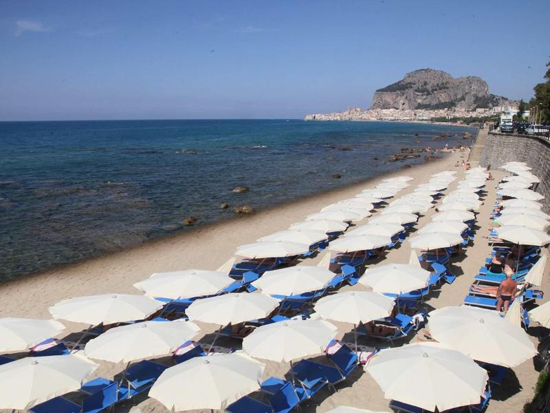 Plage avec parasols blancs et chaises longues bleues le long de la côte maritime claire sous un ciel clair.