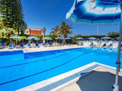Piscina all'aperto luminosa con ombrelloni blu e lettini sotto un cielo limpido.