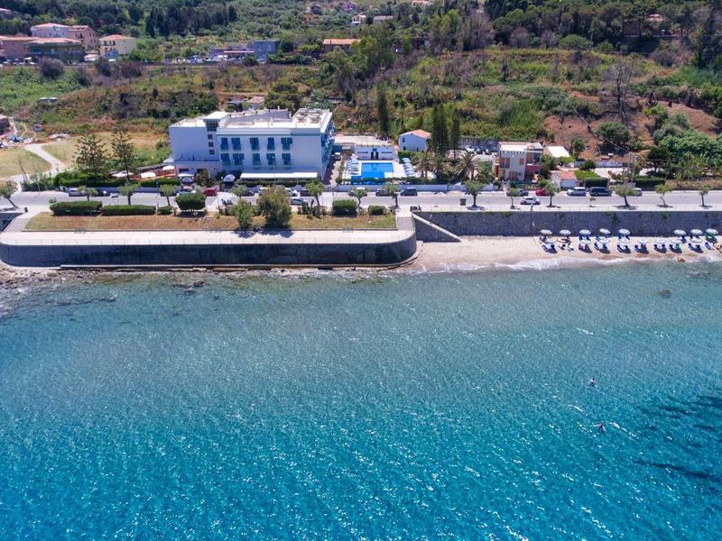 Hotelový komplex u moře s písčitou pláží, lehátky a čistou modrou vodou