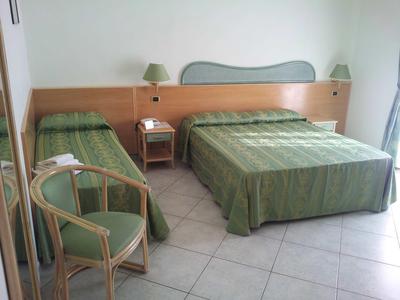 Camera d'hotel con due letti, copriletti verdi e una sedia accanto al comodino.