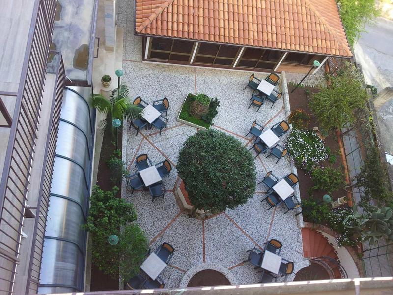 Vista dall'alto di un cortile lastricato di un hotel o caffè con tavoli e sedie intorno a un albero.