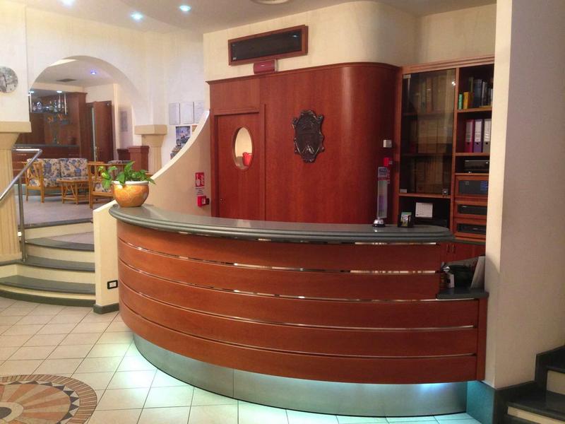 Reception con bancone in legno curvo e libreria sullo sfondo.
