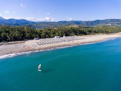 Playa de arena ancha con tumbonas, rodeada de colinas verdes y mar azul.