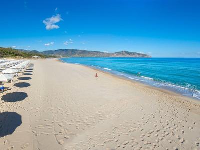 Playa de arena vacía con sombrillas a la izquierda y cielo y mar azul claro a la derecha.