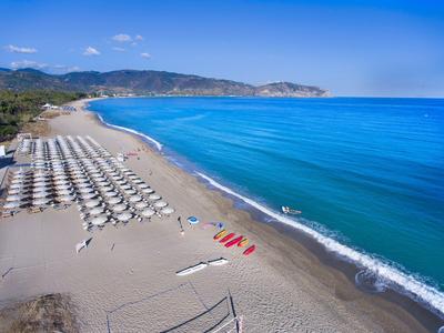 Playa con sombrillas, mar azul tranquilo y montañas en el horizonte bajo un cielo despejado.