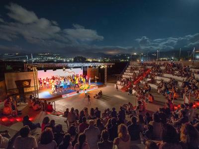 Wieczorne wydarzenie ze sceną i publicznością na otwartym amfiteatrze pod pochmurnym nocnym niebem.