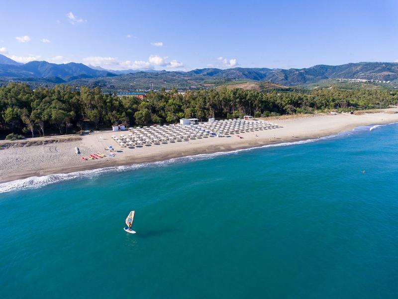 Playa de arena ancha con tumbonas, rodeada de colinas verdes y mar azul.
