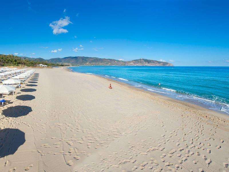 Playa de arena vacía con sombrillas a la izquierda y cielo y mar azul claro a la derecha.