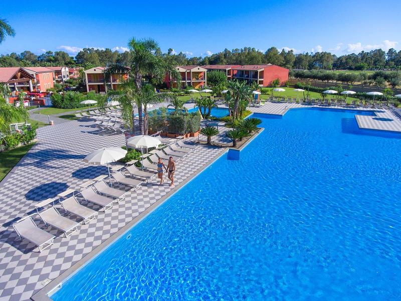 Gran piscina del hotel con tumbonas alrededor, palmeras y huéspedes paseando.