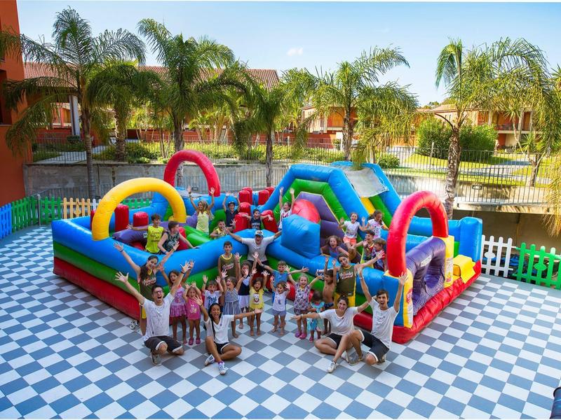 Niños juegan en un castillo inflable colorido en un área exterior del hotel con palmeras.
