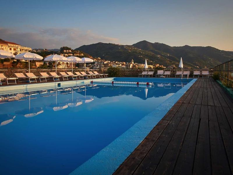 Large pool with sun loungers and mountain view at sunset.