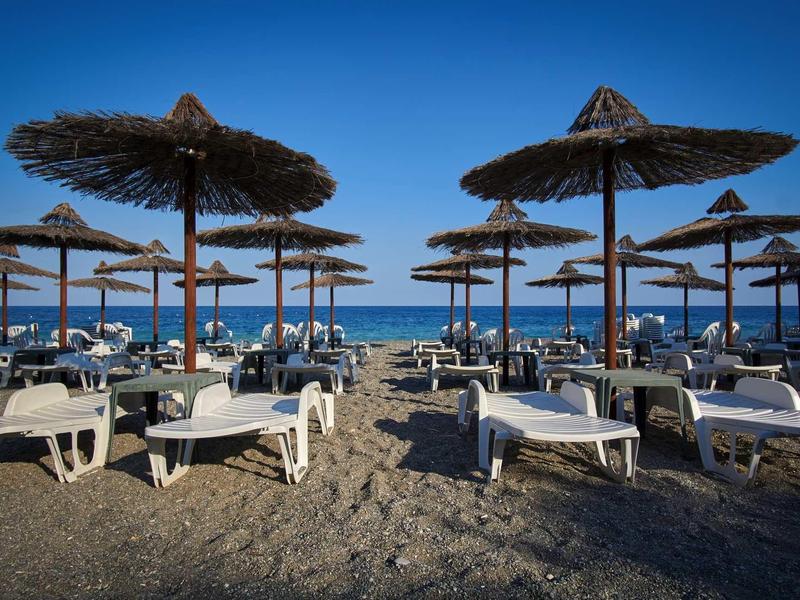 Beach view with sun umbrellas and lounge chairs under a blue sky by the sea.
