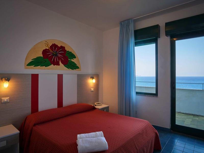 Small hotel room with double bed, window overlooking the sea, and red bedspread.