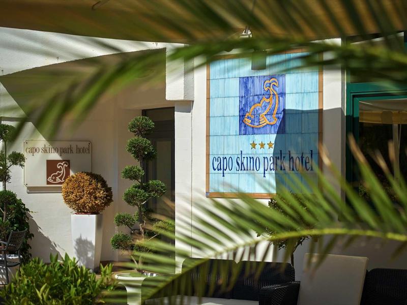 Exterior view of a hotel with decorative plants and a sign displaying the hotel name.