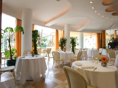 Světla restaurace s kulatými stoly, bílými ubrusy a velkými okny s rostlinami