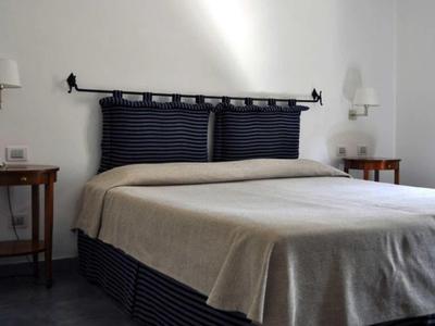 Jednoduchý hotelový pokoj s manželskou postelí, dvěma nočními stolky a bílými zdmi.