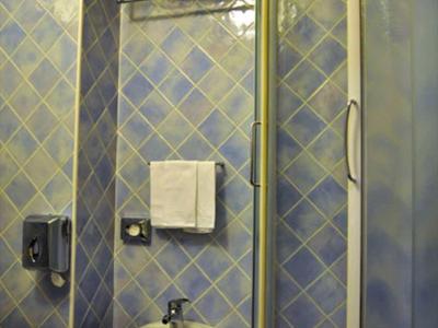 Koupelna s modrými dlaždicemi, sprchovým koutem, bidetem a ručníky na stěně.