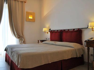 Dvoulůžkový pokoj s červenými čely postele, béžovými přikrývkami a nočními stolky s lampami.