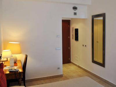 Světý hotelový pokoj s psacím stolem, židlí, lampou a velkým zrcadlem na zdi.