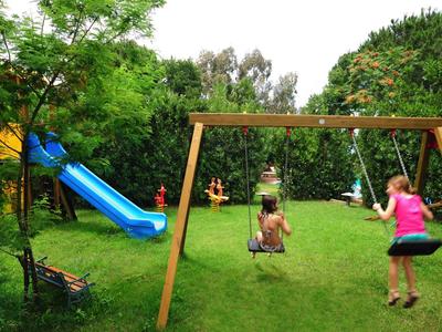 Enfant et adulte jouant sur un toboggan bleu et une balançoire dans un jardin vert.