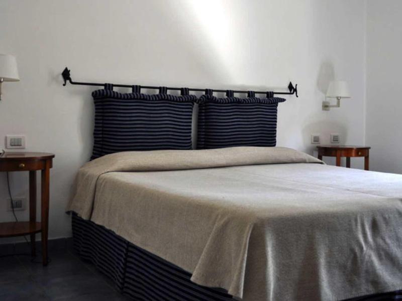 Jednoduchý hotelový pokoj s manželskou postelí, dvěma nočními stolky a bílými zdmi.