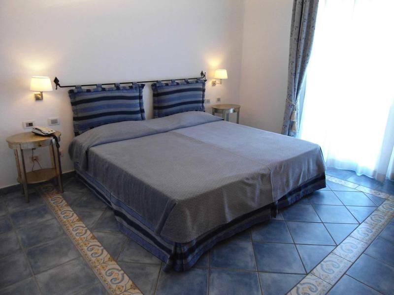 Elegantní hotelový pokoj s manželskou postelí, nočními stolky a dlažbou s kobercem