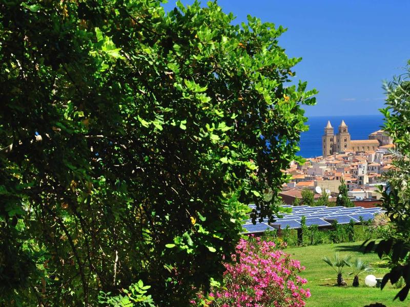 Výhled na kostel u moře skrz zelené stromy a zahradu s květinami