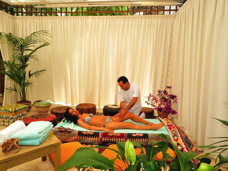 Muž dostává masáž zad v světlé spa místnosti obklopené rostlinami a závěsy.