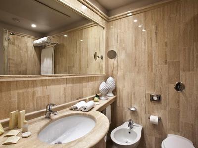 Moderní koupelna s umyvadlem, velkým zrcadlem a bidetem v teplých dřevěných tónech.