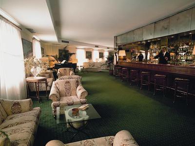 Elegantní hotelový salon s zeleným kobercem, květinovým čalouněním a dlouhým barem s barovými židlemi.