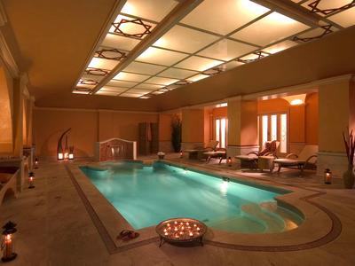 Osvětlený krytý bazén s lehátky v luxusní wellness oblasti.