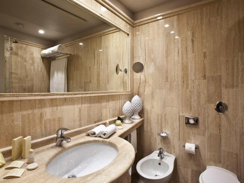 Moderní koupelna s umyvadlem, velkým zrcadlem a bidetem v teplých dřevěných tónech.