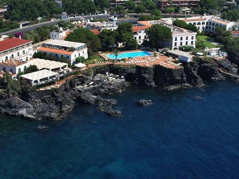 Hotelový komplex na skalnatém pobřeží s čistou tmavě modrou vodou a bazény.