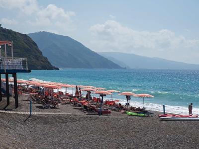 Strand mit Liegestühlen, Sonnenschirmen und Bergen im Hintergrund am Meer