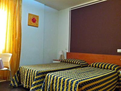 Twin room with striped bedcovers, chair, and yellow curtains in a hotel.