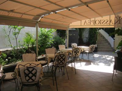 Outdoor seating area with chairs and tables under an awning surrounded by plants.