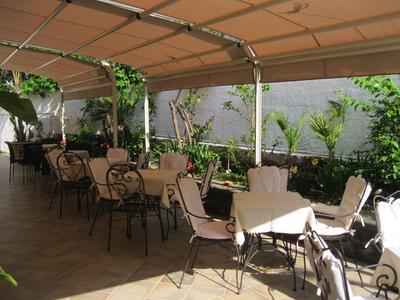 Covered outdoor area with tables and chairs, surrounded by plants and natural light.