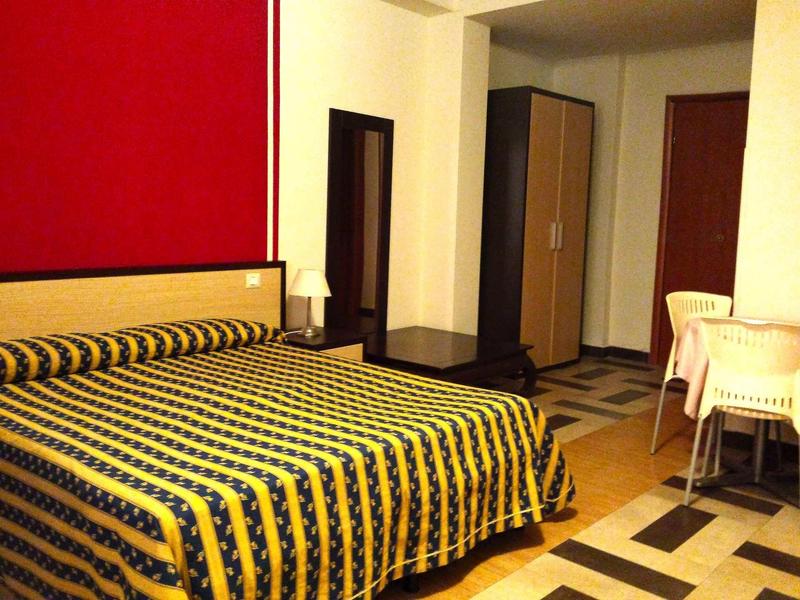 Hotel room with large bed, floor lamp, mirror, and table with chairs.