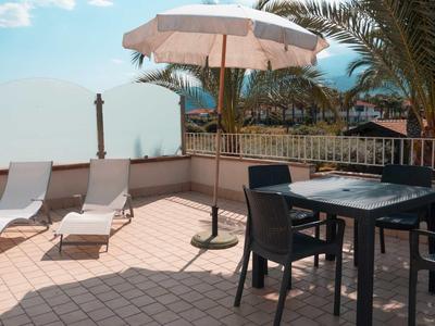 Terraza con tumbonas, mesa, sillas y sombrilla bajo cielo azul