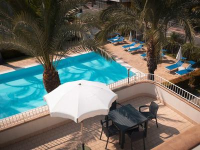 Vista de una zona de piscina con palmeras, tumbonas y una mesa con sombrilla.