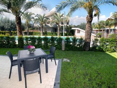 Terraza con mesa y sillas junto a un jardín verde con palmeras