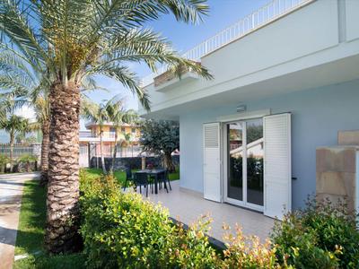 Modern hotel bungalow with terrace, palm trees, and well-kept garden under clear sky.