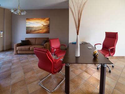 Sala de reuniones moderna con dos sillas rojas, sofá marrón y pintura de paisaje natural en la pared.